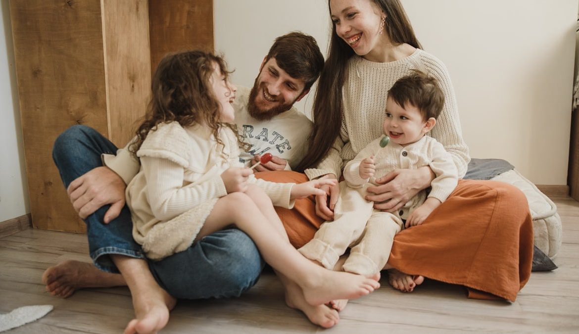 Smiling family of four sitting on the living room floor, enjoying quality time together.