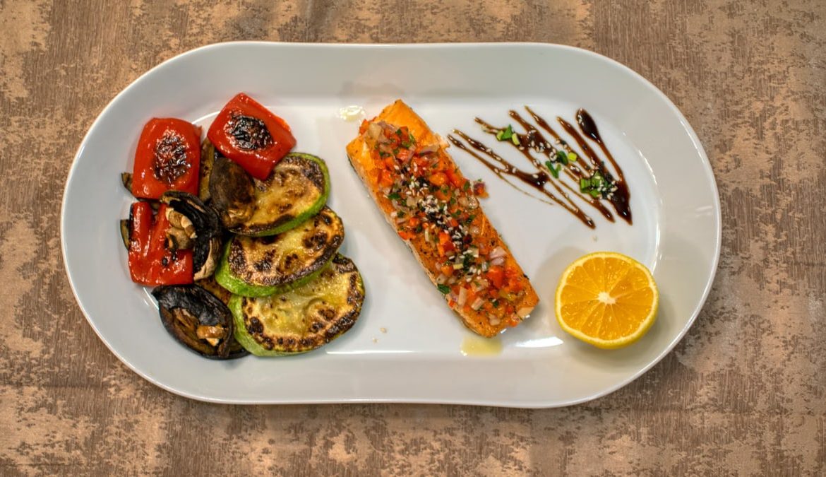Gourmet grilled salmon served with roasted vegetables and lemon slice on a white plate.
